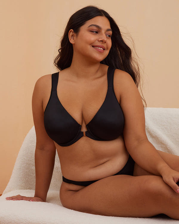 Woman wearing a black bra and underwear set against a beige background